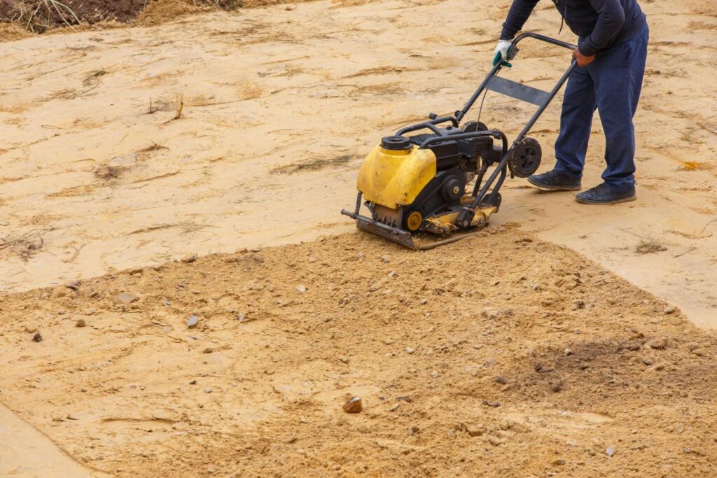 Ouvrier utilisant un compacteur à main pour tasser le sol lors des travaux de terrassement