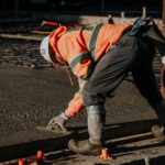 Un ouvrier en tenue de sécurité lisse du béton fraîchement coulé sur un chantier de construction.