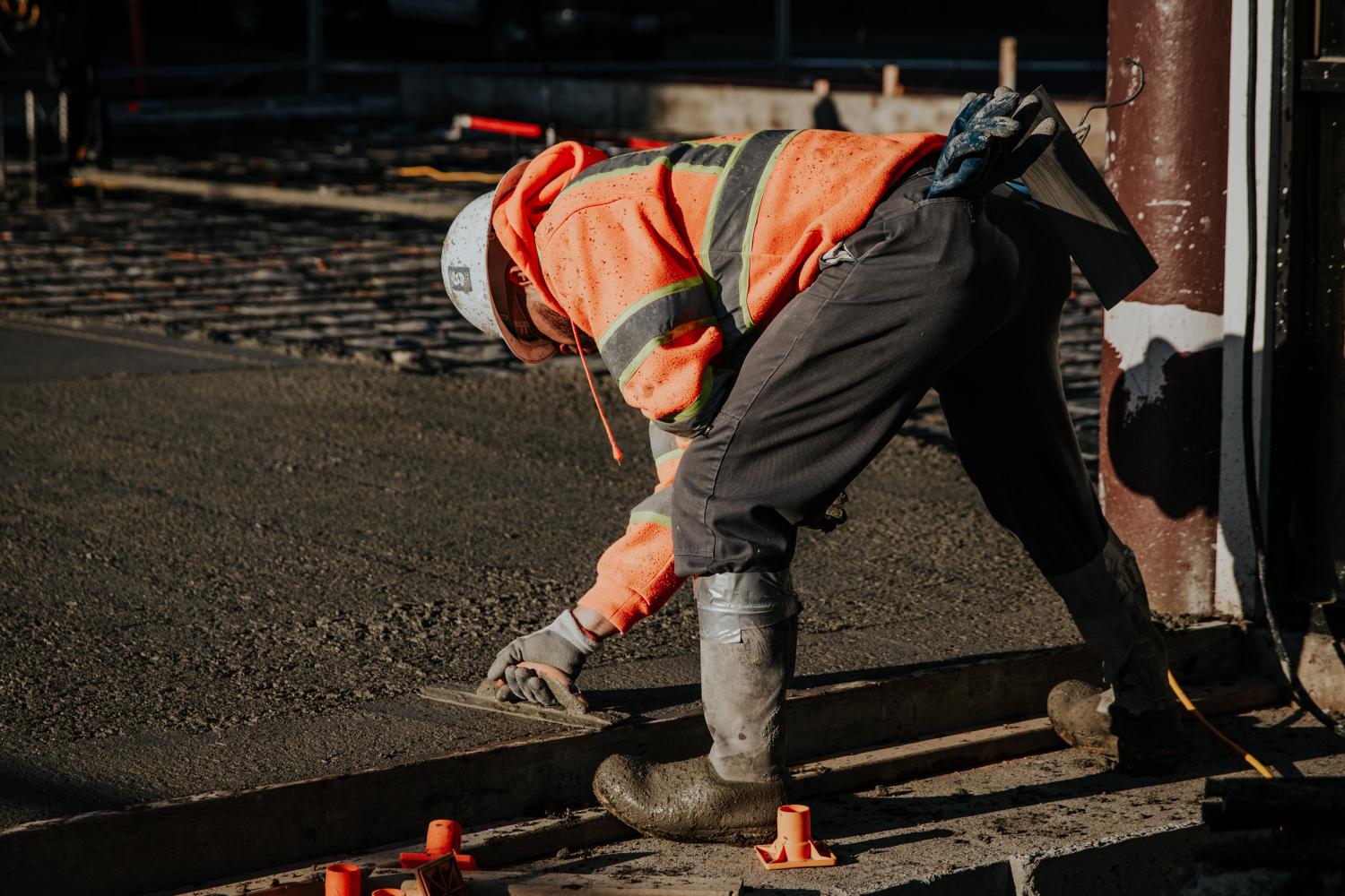 Un ouvrier en tenue de sécurité lisse du béton fraîchement coulé sur un chantier de construction.